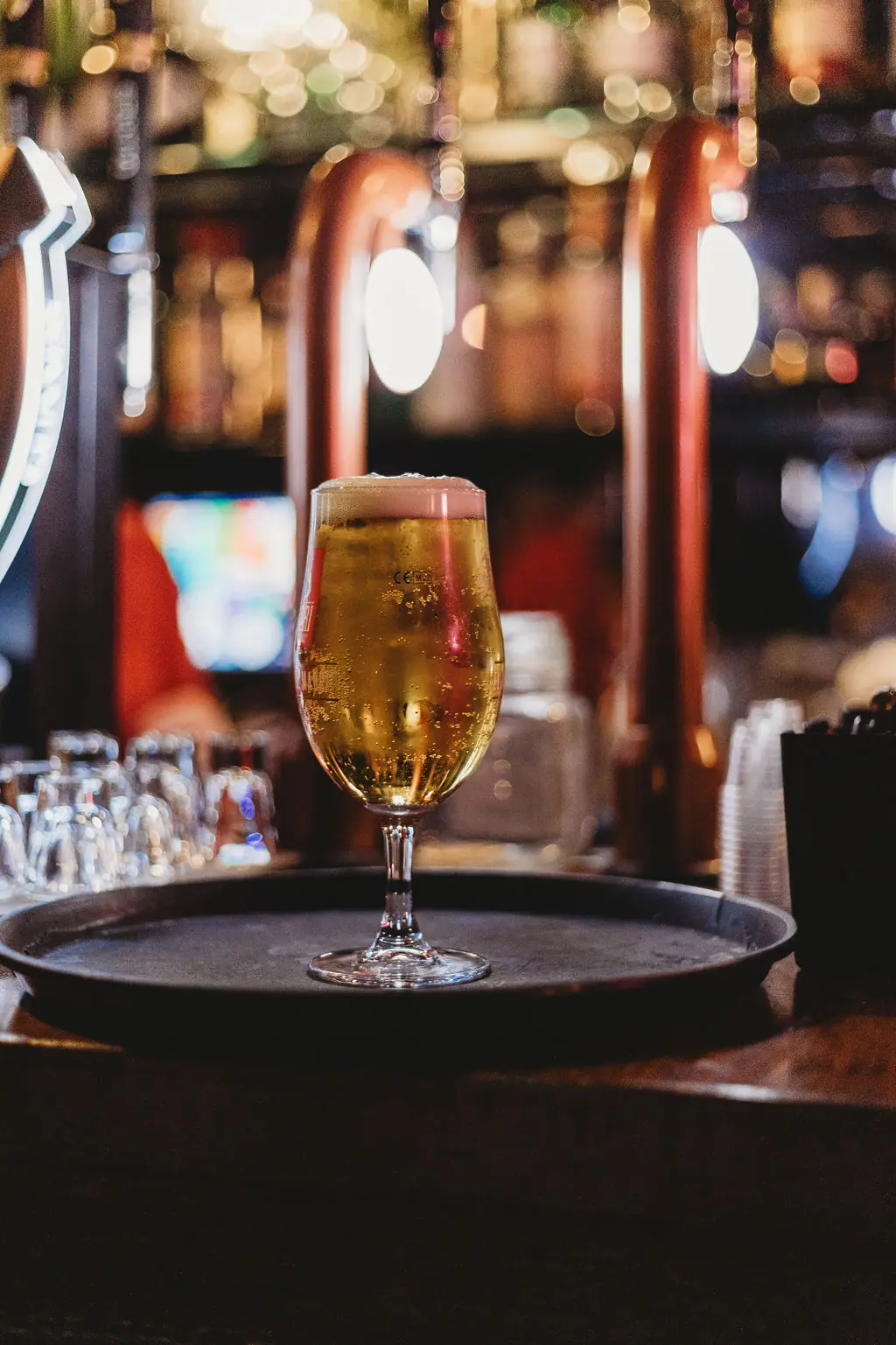 A freshly poured lager on a bar tray in front of copper beer taps
