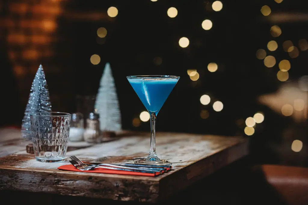 A blue cocktail on the edge of a table with Christmas lights behind