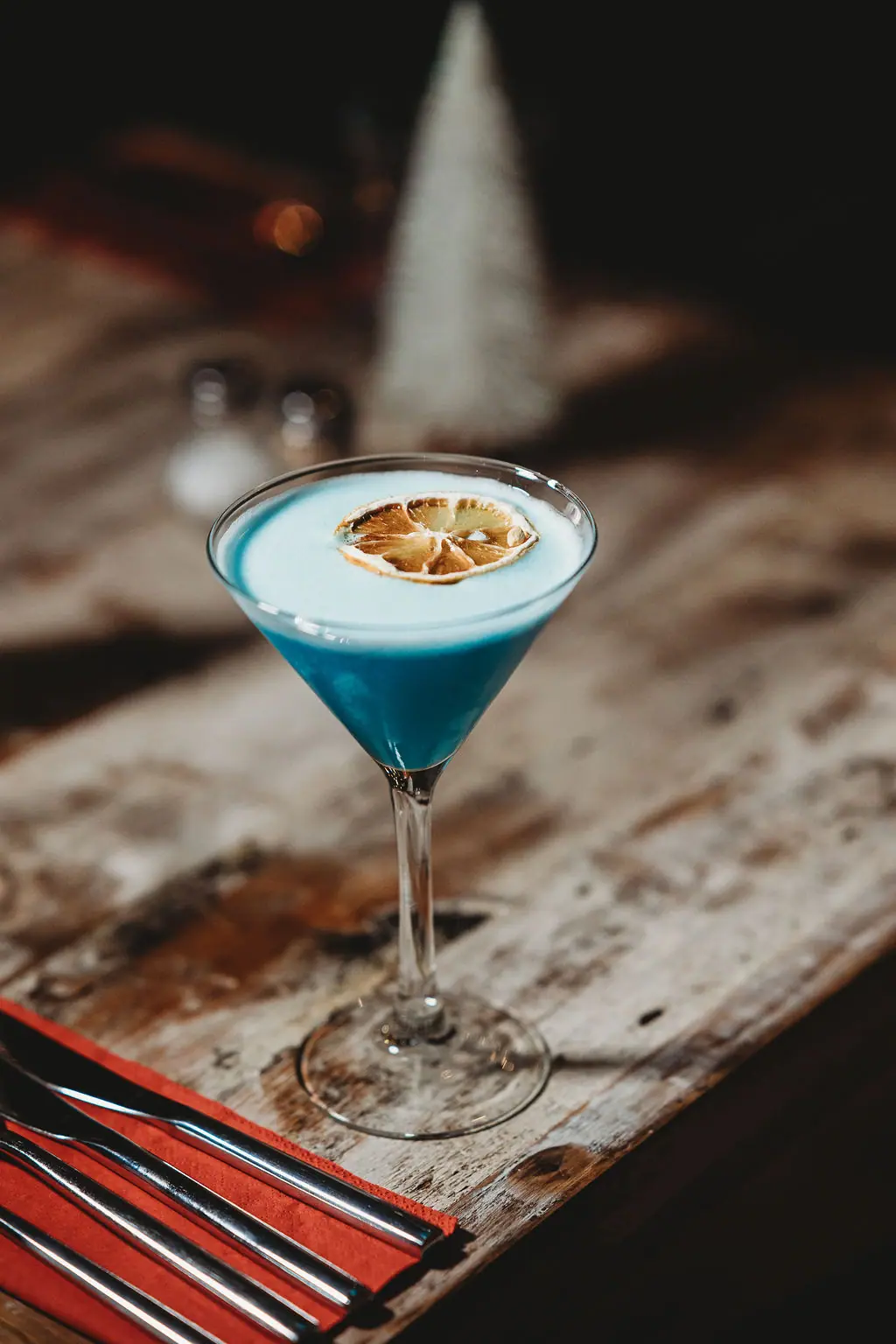 The Teal Monkey cocktail with a dried lemon wheel on a wooden table