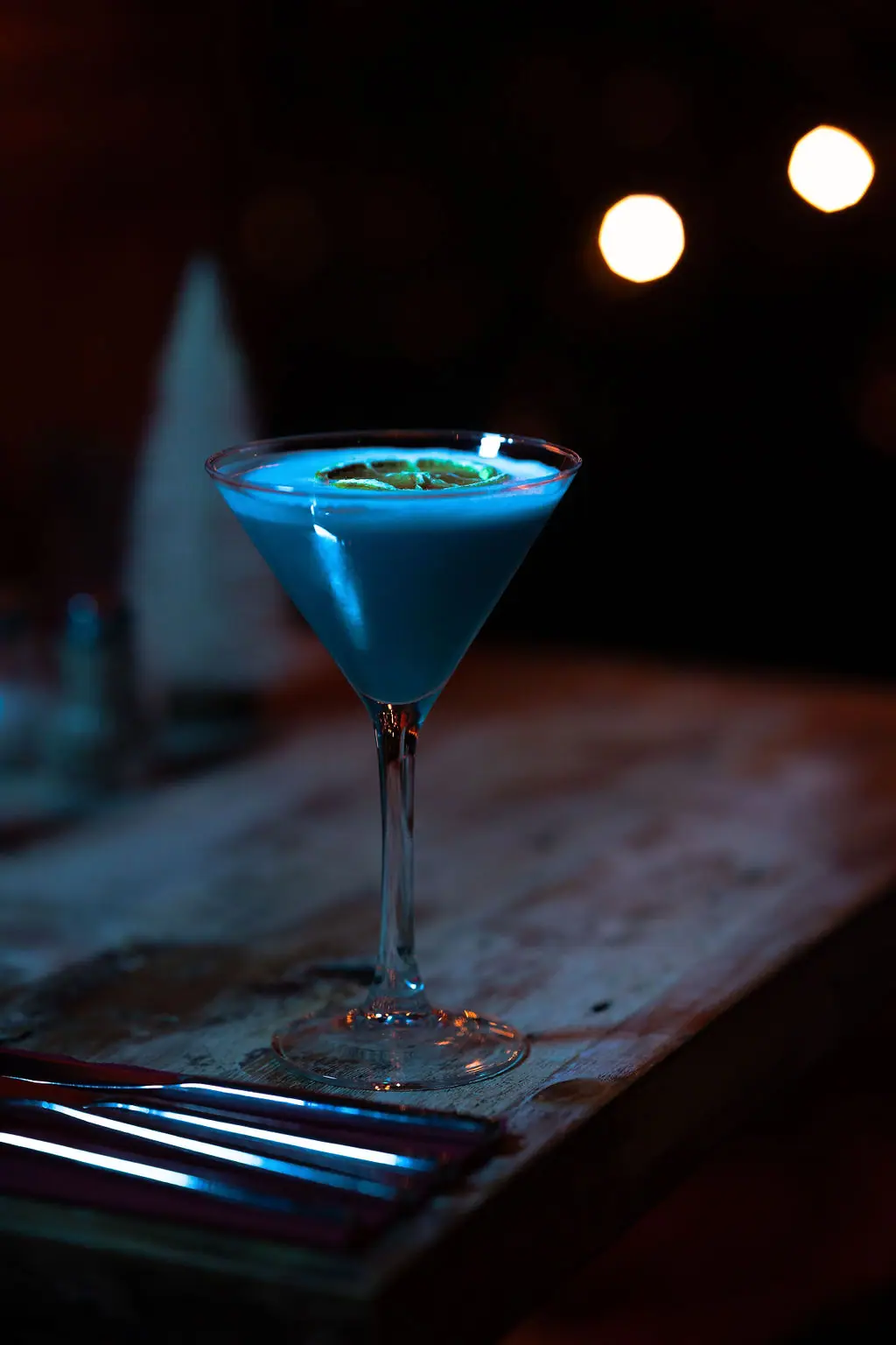 The Teal Monkey signature cocktail glowing blue on a rustic table, fairy lights behind