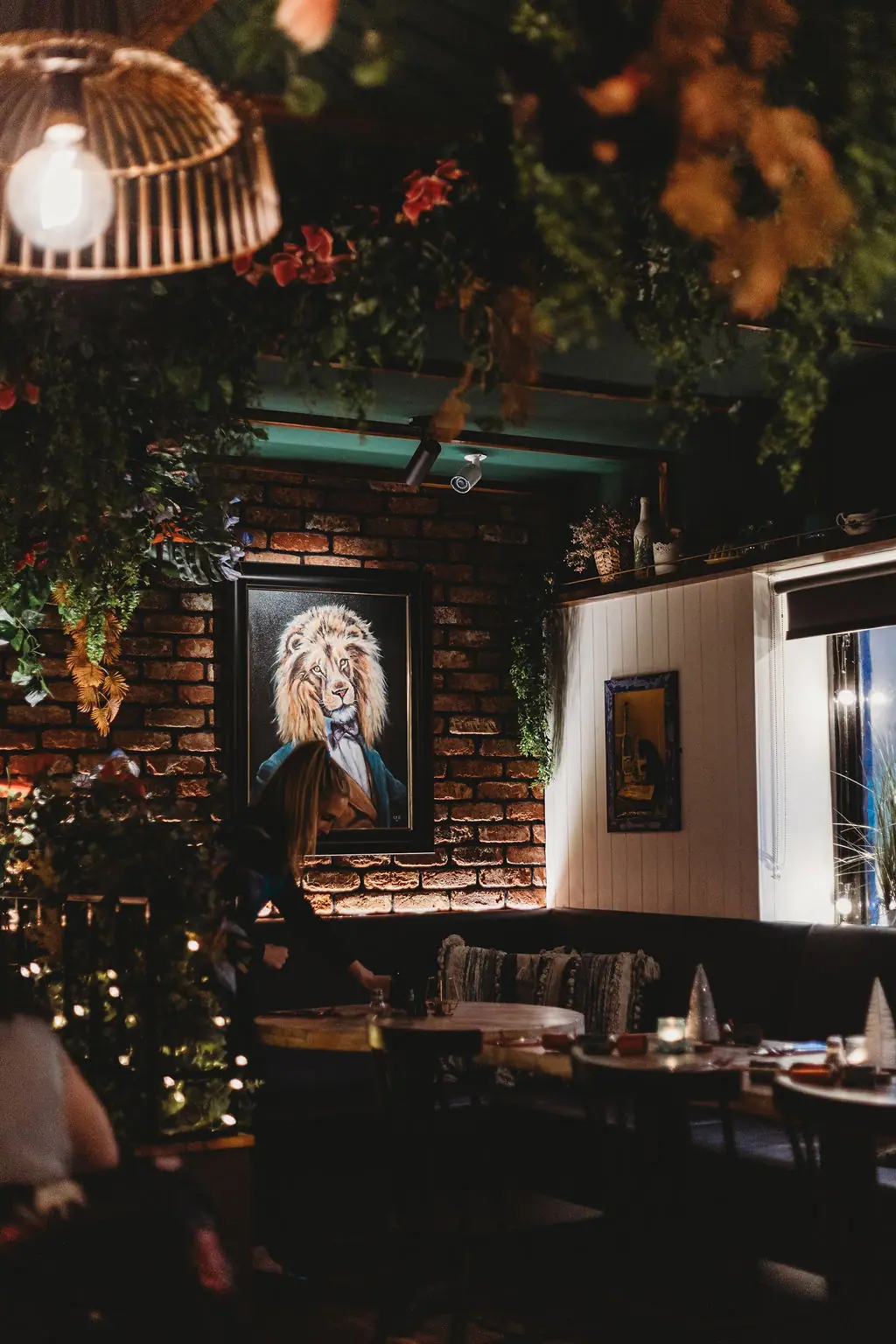 The Teal Monkey dining room at night, lion portrait above a booth and foliage overhead
