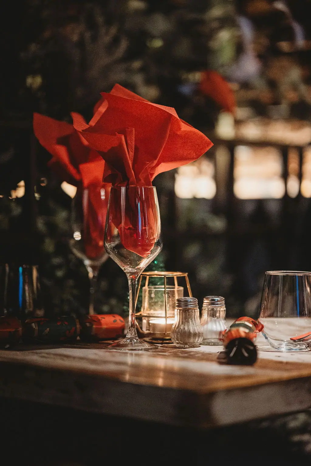 A wine glass holding a folded red napkin beside a candle on a set table