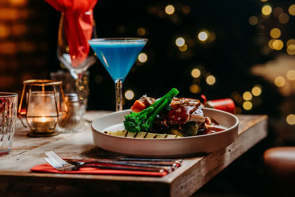 A Christmas plate with tenderstem broccoli and a blue cocktail on a dressed table